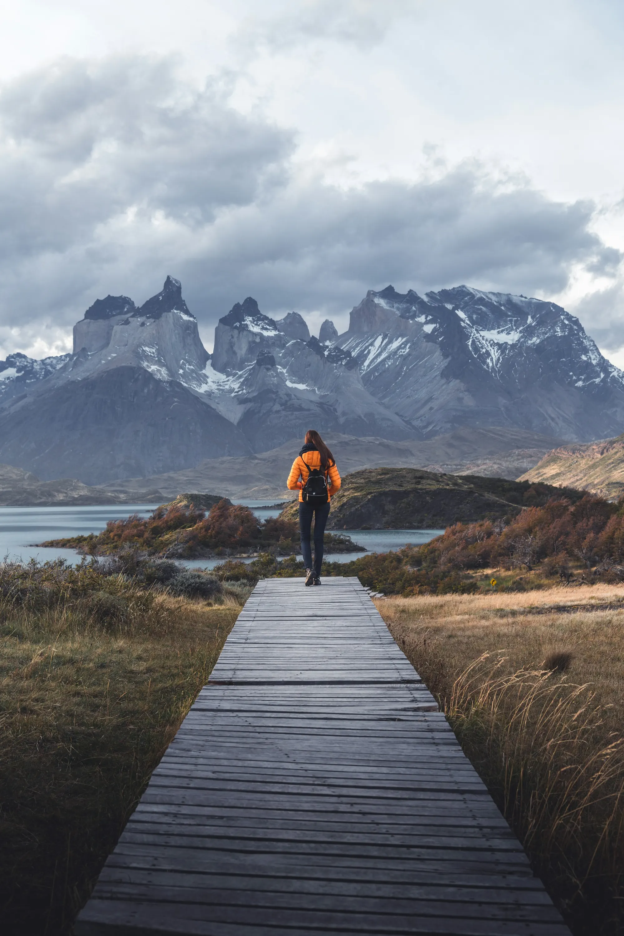 Hiker on a boardwalk trail facing Torres del Paine mountains in Patagonia