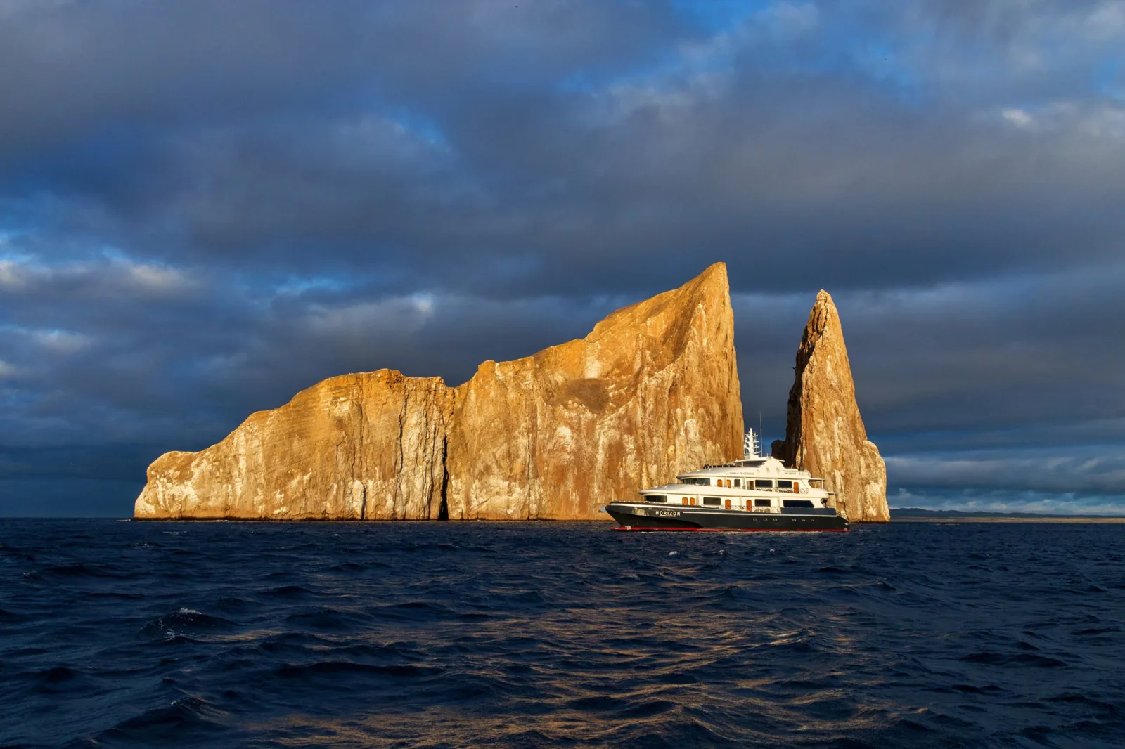 A small expedition ship beside the towering Kicker Rock formation in the Galápagos at golden hour