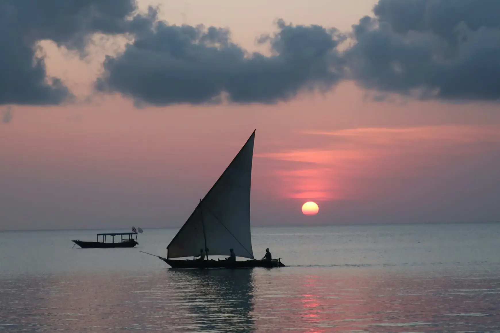 Traditional dhow sailboat silhouetted against a vivid Indian Ocean sunset off Zanzibar