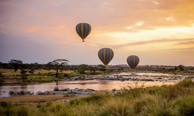 Hot air balloons drifting over the Serengeti river at golden-hour sunrise